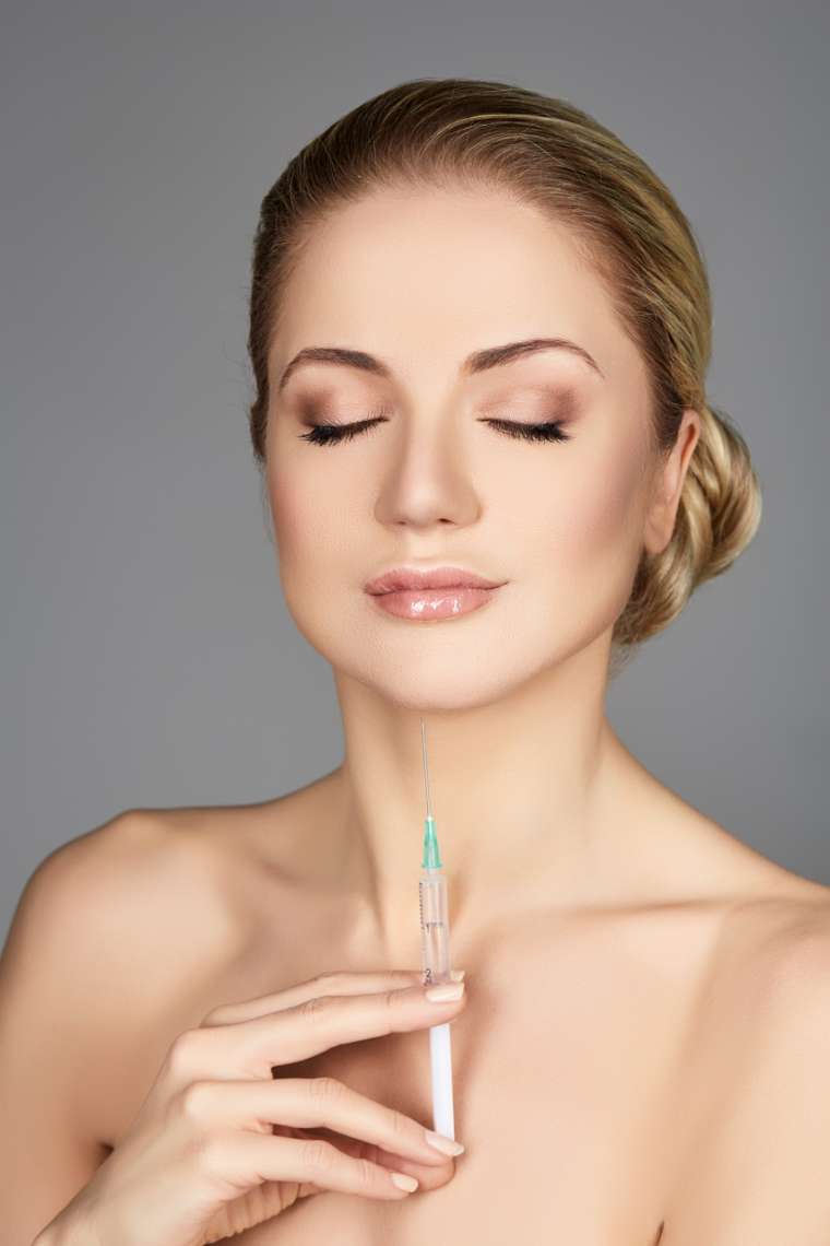 beautiful young woman holding syringe with collagen treatment injection. beauty shot on grey background. copy space.